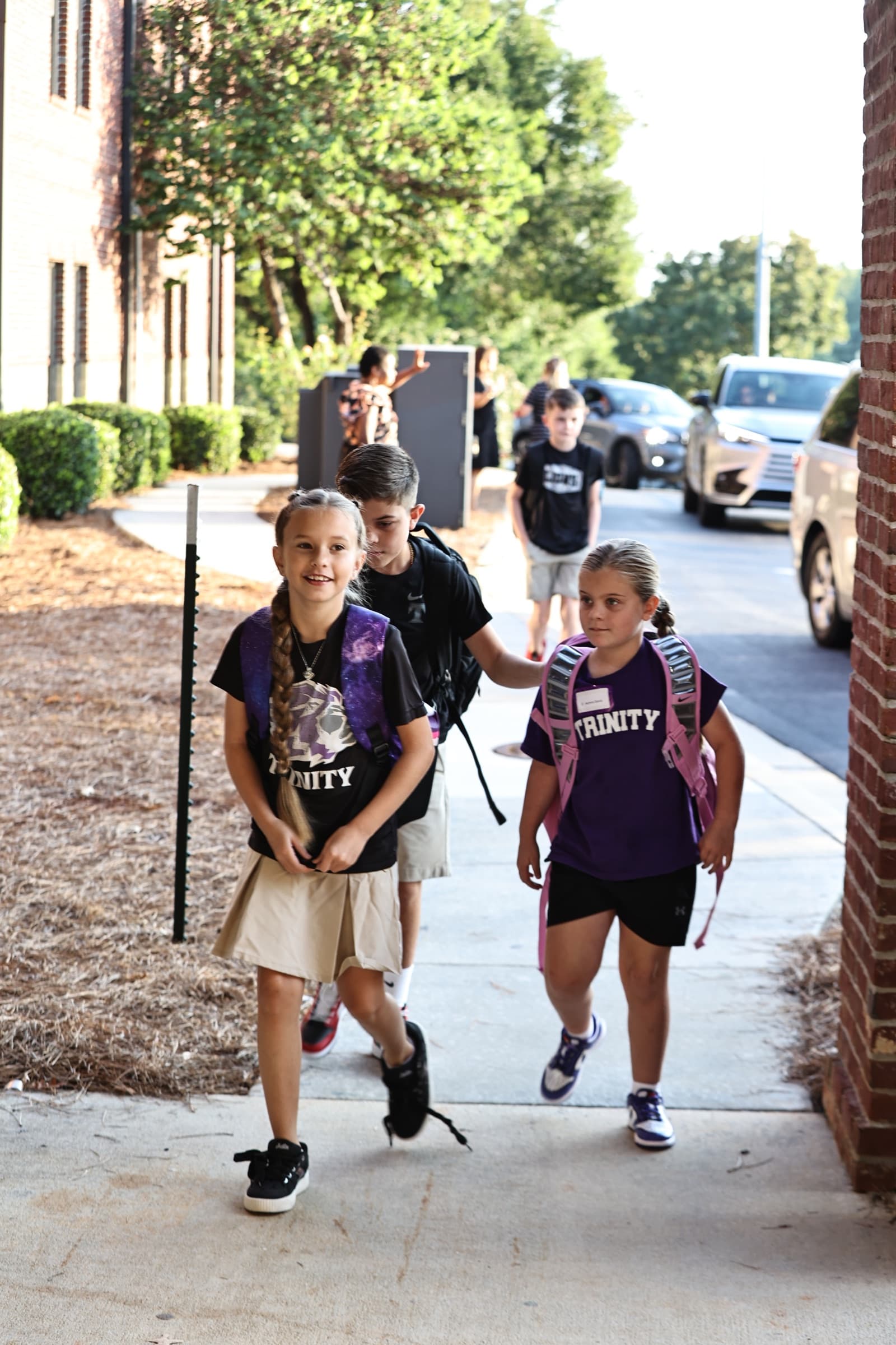 Smiling upper-elementary TCS students walking toward the school entrance with backpacks