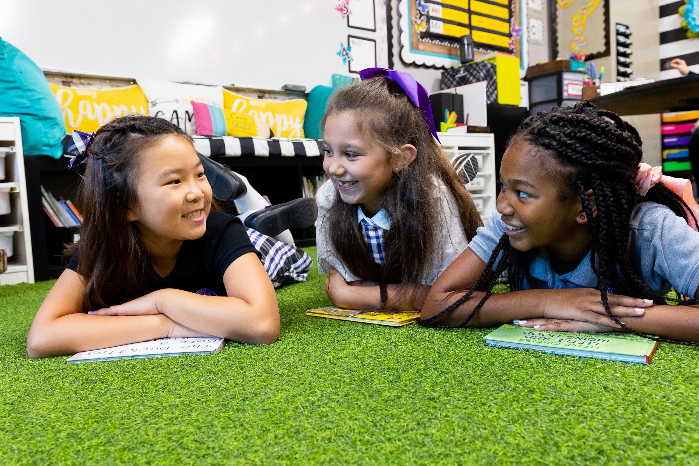 Three smiling TCS students sharing books and conversation in a classroom